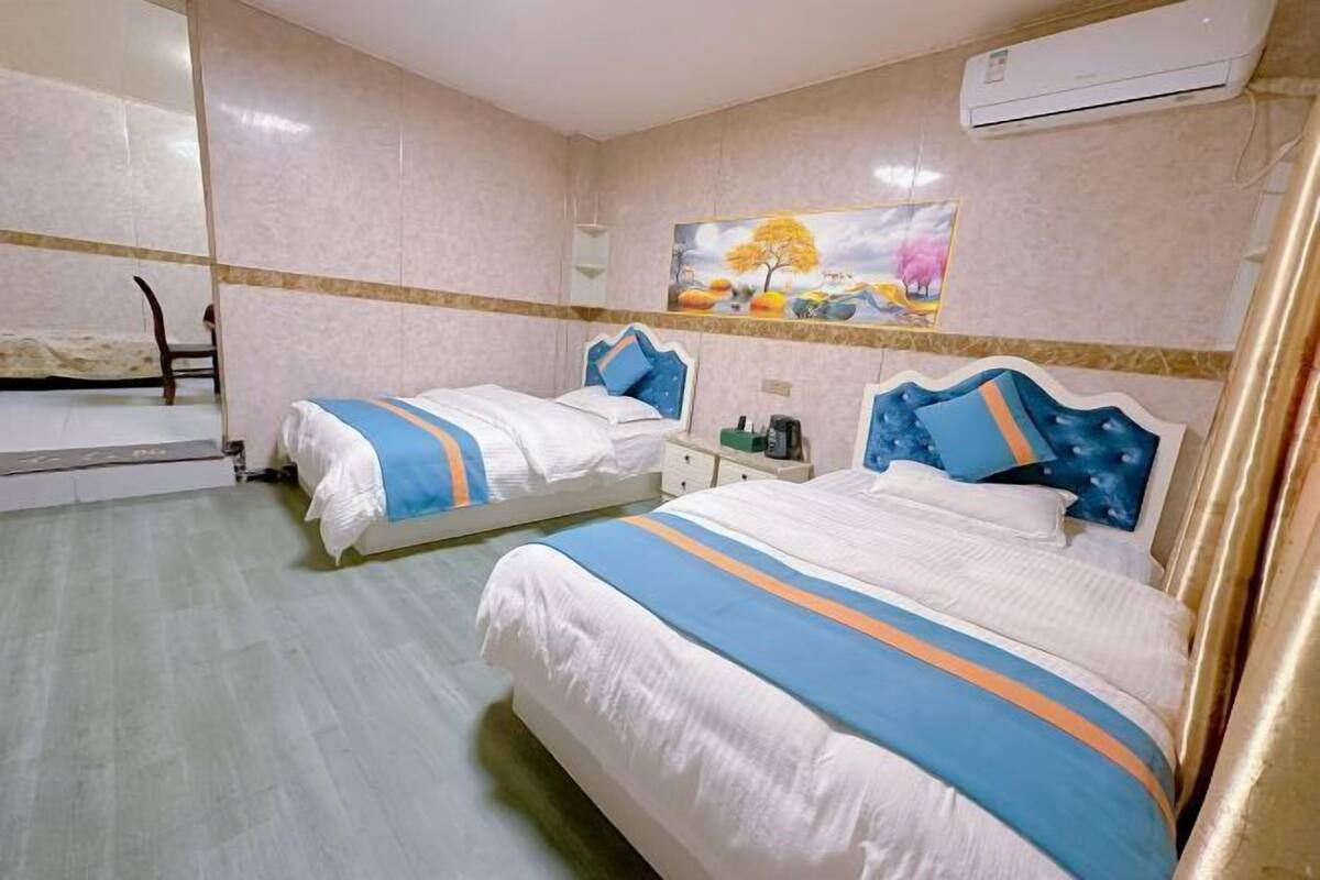 Une chambre d’hôtel avec deux lits, une petite table, une chaise et un tableau au mur.