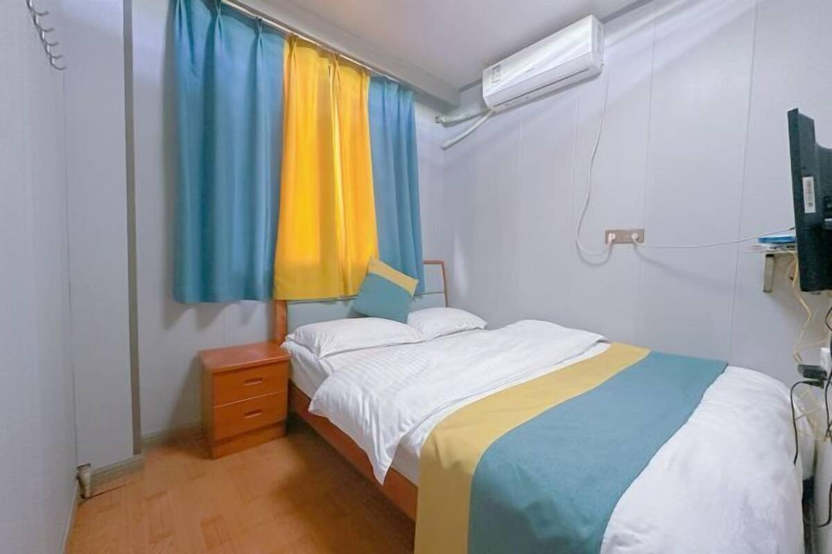 Une chambre à coucher comprenant un lit, une table de chevet, une fenêtre avec des rideaux, un appareil de climatisation et un téléviseur.