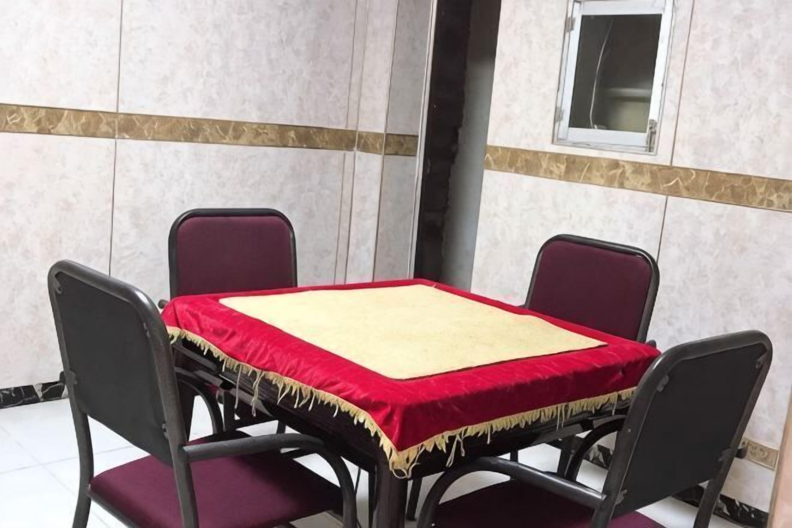 Una mesa de conferencias con mantel rojo, cuatro sillas y una ventana pequeña encima.