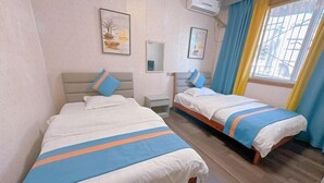 Een hotelkamer met twee bedden, elk met een blauw-oranje gestreept dekbedovertrek, een nachtkastje, een spiegel en een raam met blauwe gordijnen.