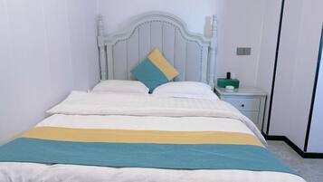 A bed with a white headboard, a teal and yellow striped blanket, and a single teal pillow.