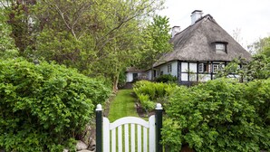 Ein traditionelles Haus mit einem Strohdach und einem Steinweg, der zu einem weißen Tor führt.