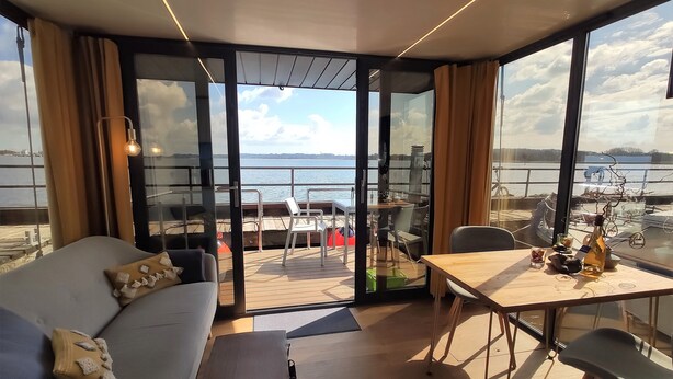 Ein modernes Zimmer mit großem Fenster, einer Couch, einem Tisch und Blick auf das Wasser.