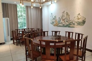 Een eetgedeelte met een ronde tafel en stoelen, een schilderij aan de muur en een raam met gordijnen.