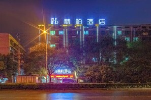 Un edificio con señalización iluminada, un estacionamiento y árboles en primer plano.