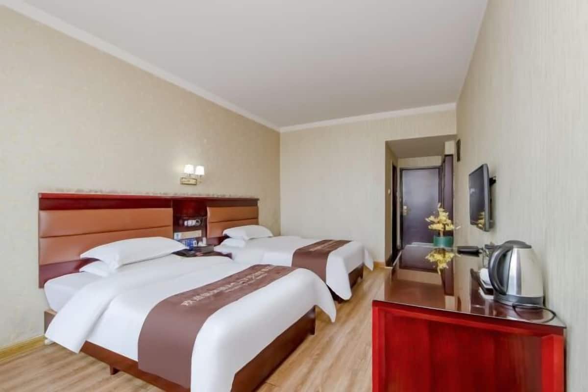 A hotel room with two beds, a wooden headboard, a desk with a mirror, and a coffee maker.