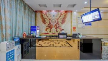 A hotel reception area with a reception desk, a digital screen, and a decorative wall.