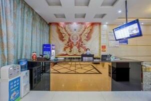 A hotel reception area with a reception desk, a digital screen, and a decorative wall.
