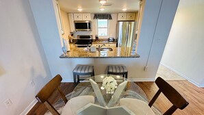 Una cocina moderna con encimeras de granito, electrodomésticos de acero inoxidable y un comedor con mesa y sillas de vidrio.