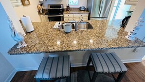 Una cocina con encimeras de granito, electrodomésticos de acero inoxidable y ventana con vista al océano.