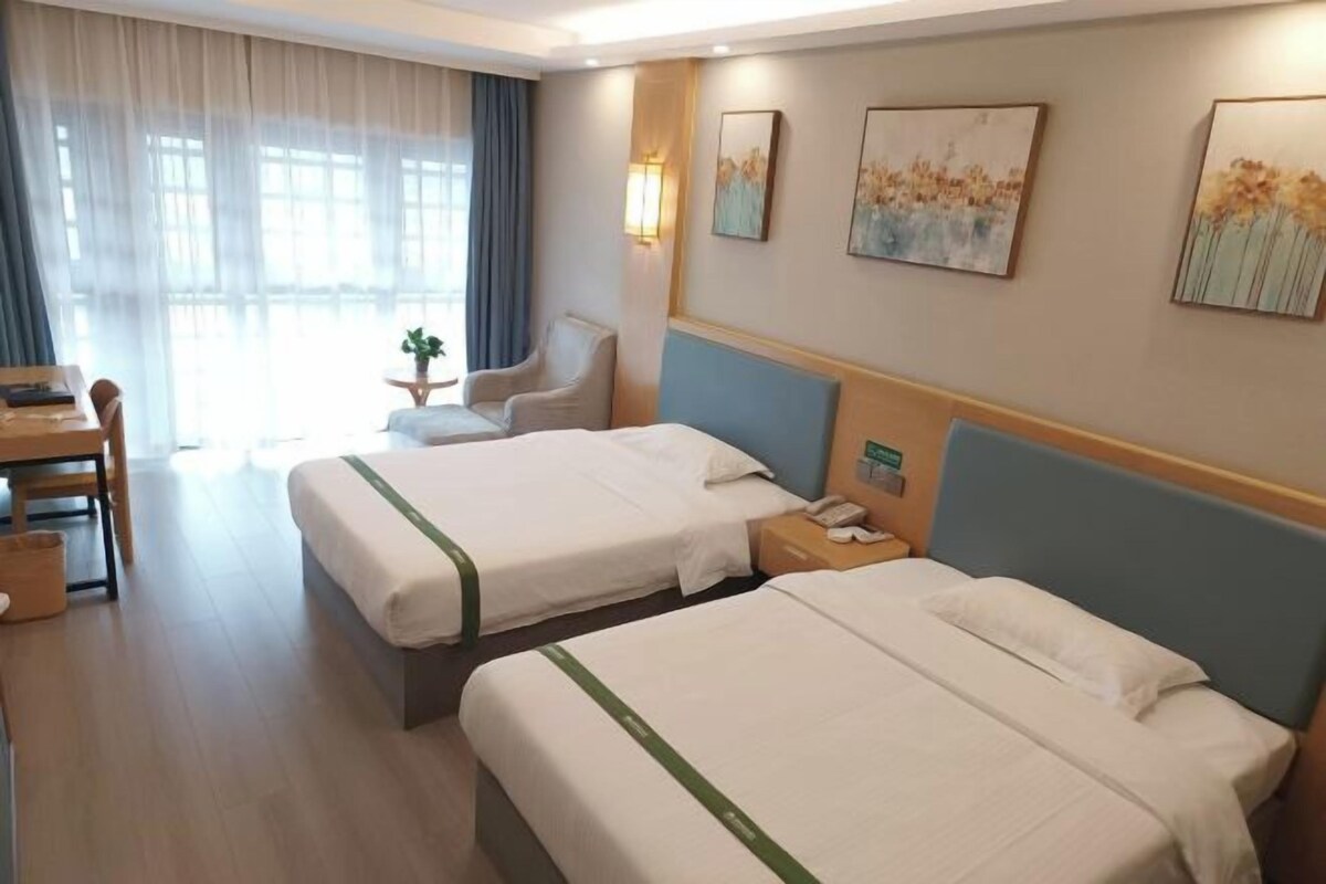 Una camera d'albergo con due letti, una scrivania e una sedia. Alle pareti ci sono dei quadri e una finestra con tende.