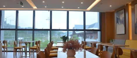 Un comedor amplio con ventanas grandes, mesas de madera y sillas amarillas.