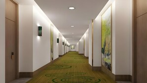 En lang, smal hotelgang med tæppe med grønne cirkulære mønstre, hvide vægge og trædøre på begge sider.