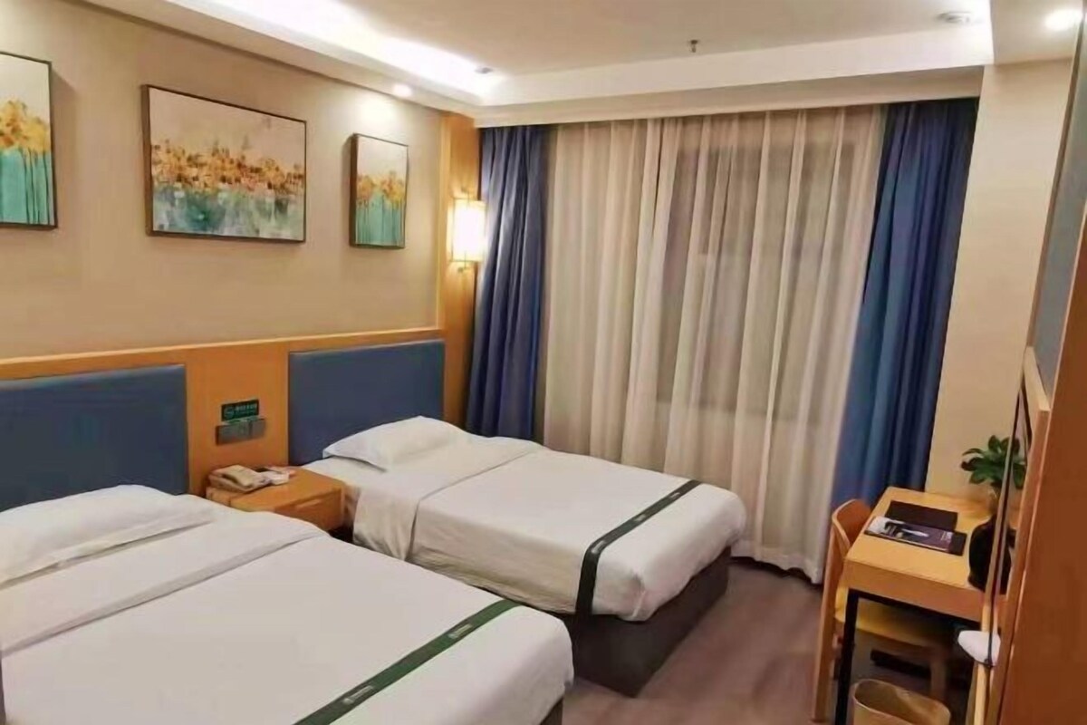 Habitación de hotel con dos camas, un escritorio, una silla y una ventana con cortinas.