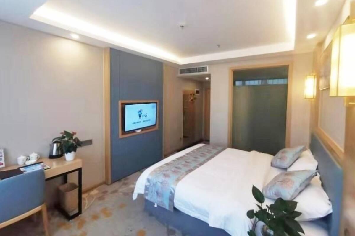 A hotel room with a bed, bedside table, and a TV mounted on the wall.