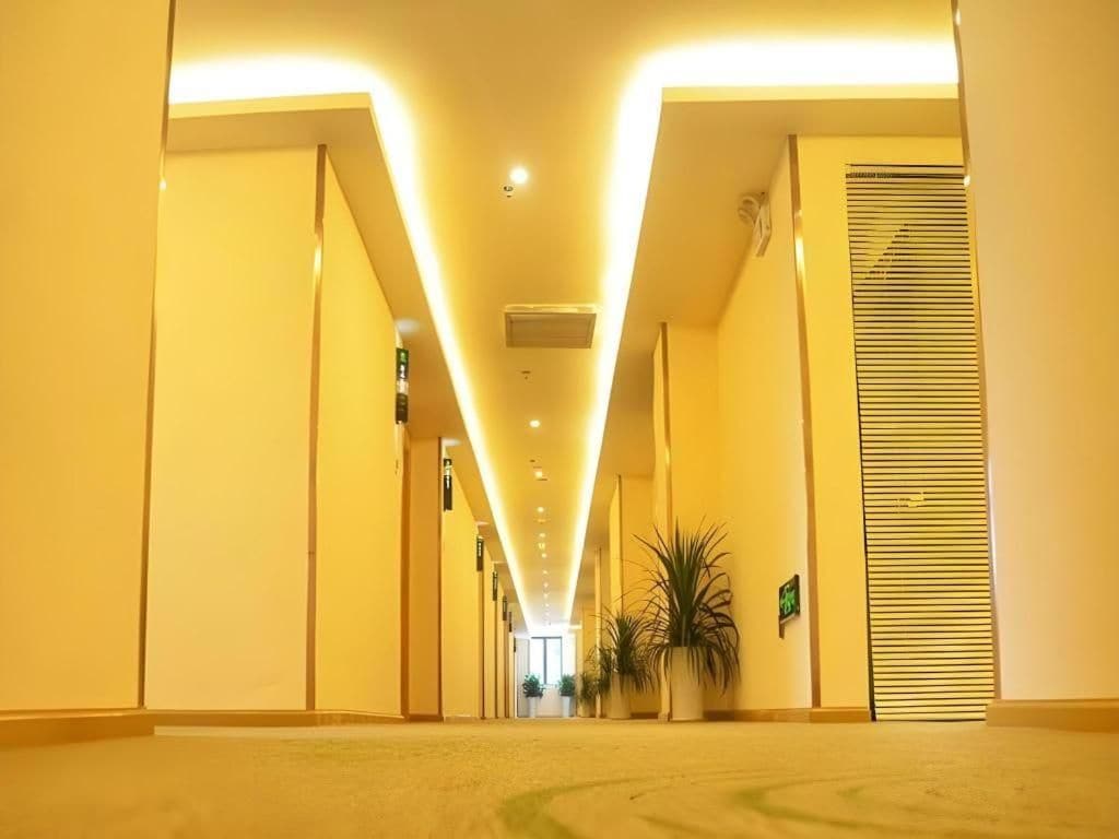 Corredor de hotel com design moderno, apresentando uma luminária central e plantas em vasos ao longo das paredes.