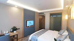 A hotel room with a bed, bedside table, TV, and a small desk with a plant. - Greentree Inn Guiyang Wudang District High-speed Railway East Station (Guiyang)
