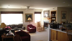 Ein Wohnzimmer mit einer Couch, einem roten Sessel, einem Holzesstzimmer und einer Küchenzeile mit Mikrowelle und Herd.