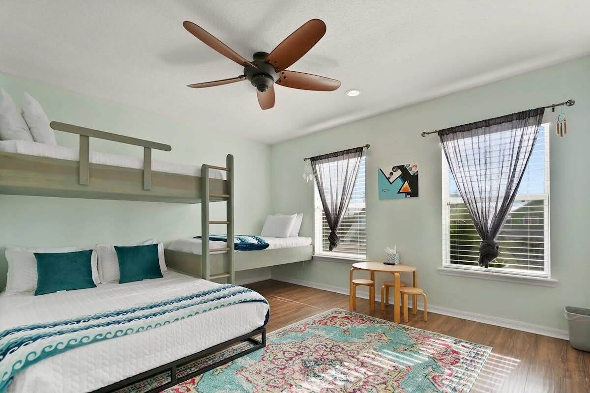 Ein Schlafzimmer mit Etagenbetten, Deckenventilator, kleinem Tisch und einem fenster mit Vorhängen.