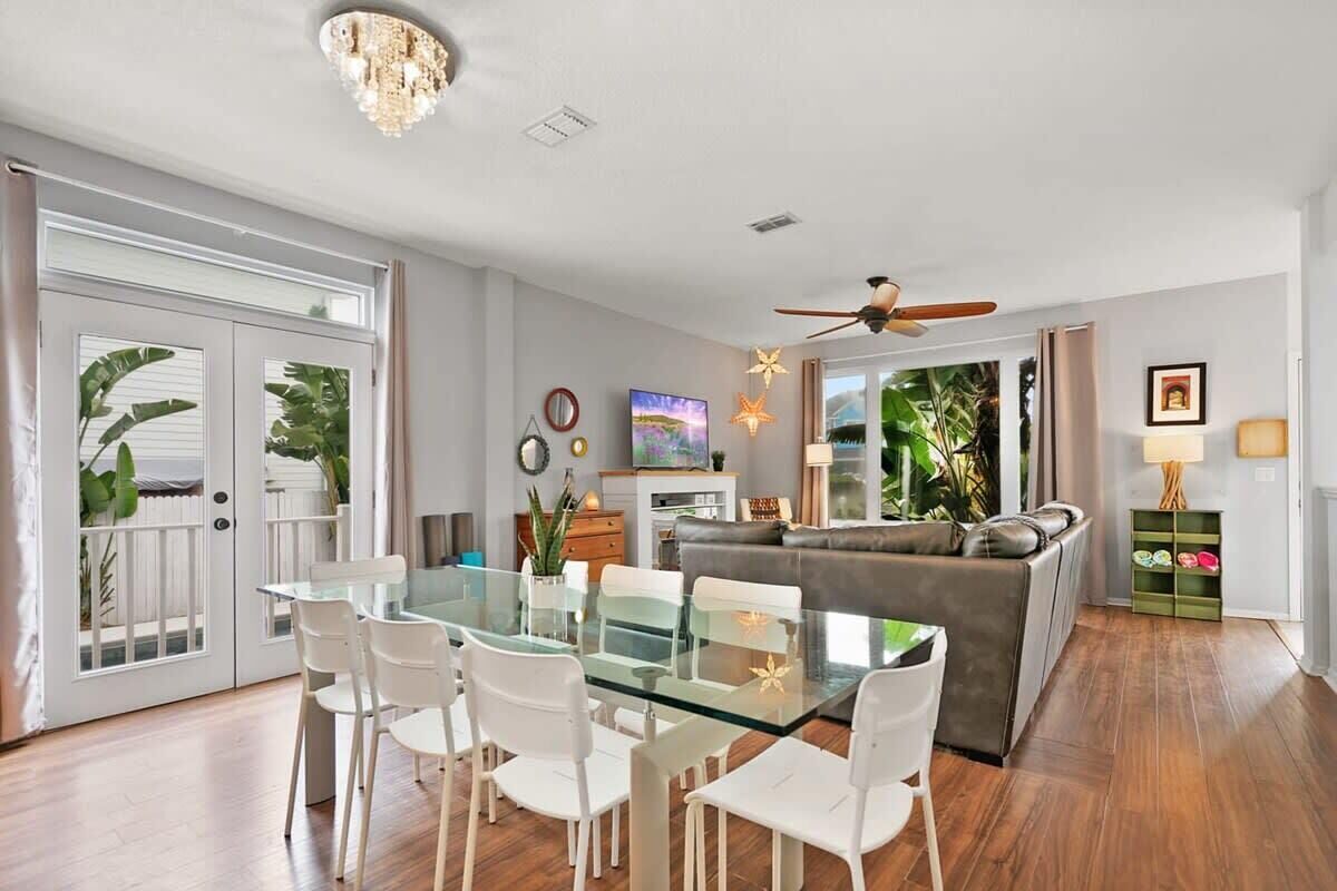 Una sala de estar moderna con una mesa de comedor de cristal, sillas blancas, un sofá gris y un ventilador de techo.