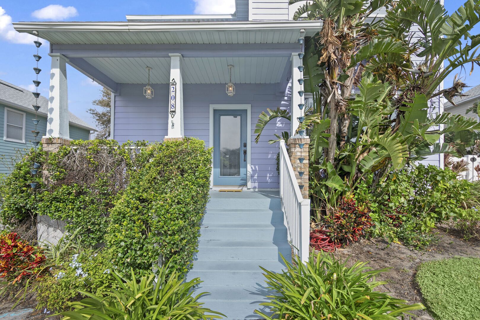 A house with a porch, a number 208 sign, and a variety of plants and flowers.