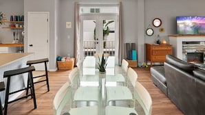 A modern living room with a glass dining table, a leather sofa, and a TV on a wooden stand. - Heated Pool, Tiki Lounge, Steps to Beach, Games (St. Augustine)