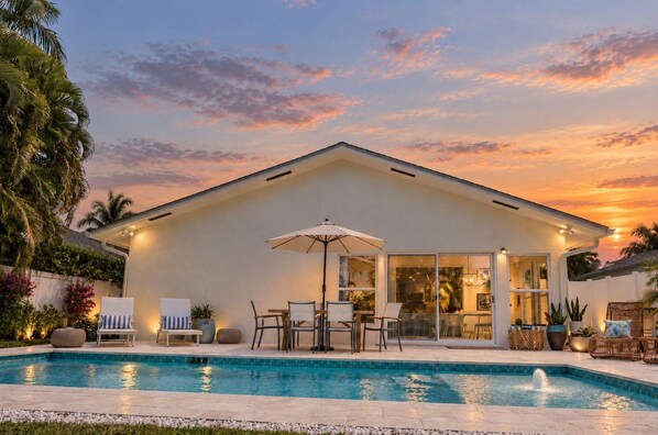 A modern house with a swimming pool, outdoor seating, and a sunset view.