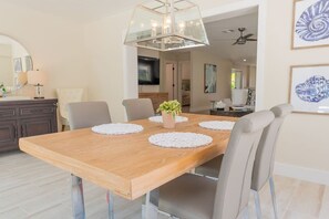 A dining area with a wooden table, six chairs, a central plant, and a modern chandelier. - 637 Palms Oasis | Heated Private Pool | Walk2Beach (Naples)