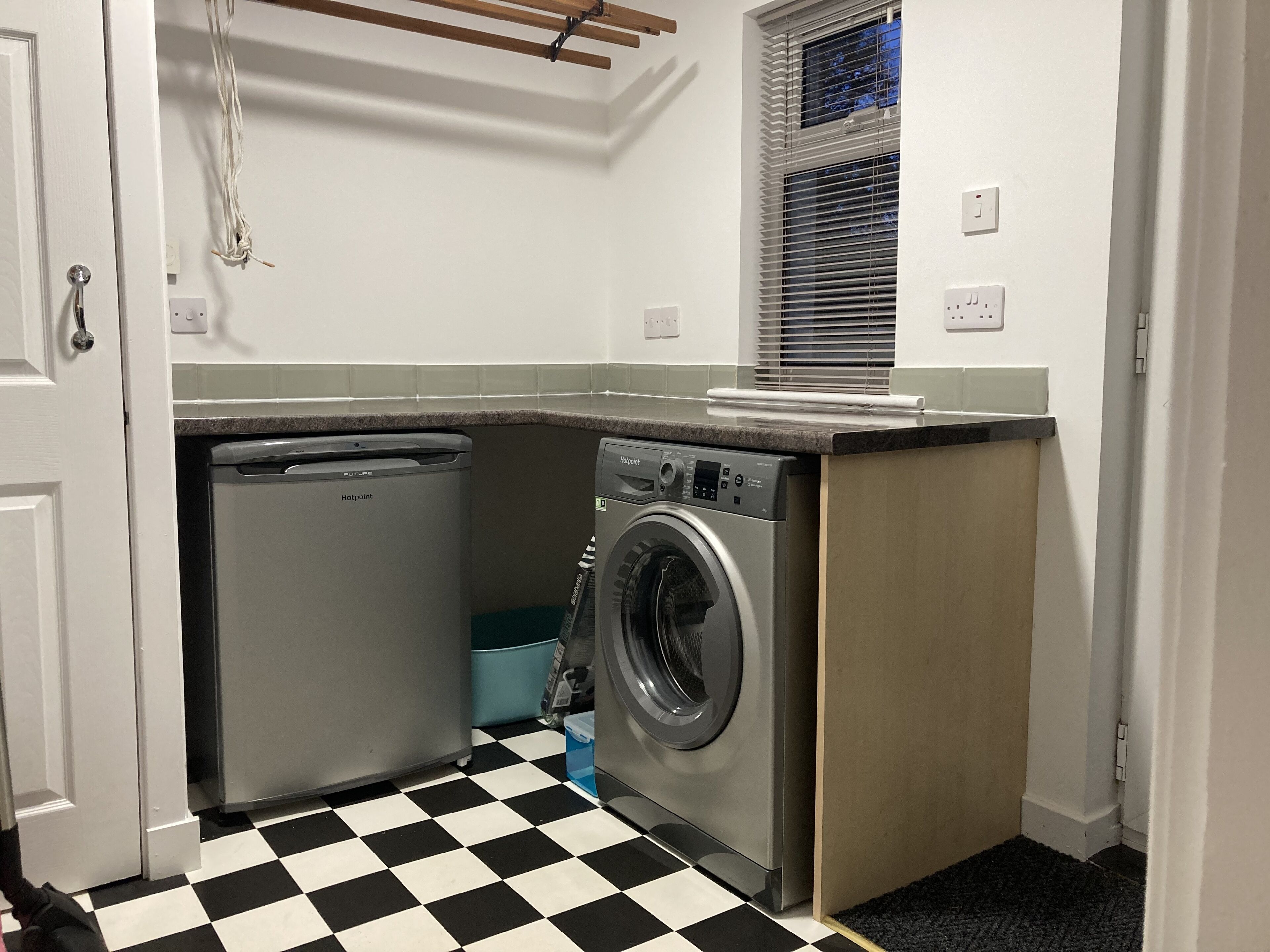 A compact laundry room with a washing machine, a compact dishwasher, and a small trash bin.
