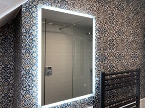 Un baño con ducha separada por una puerta de vidrio, un toallero negro y baldosas decorativas en las paredes.