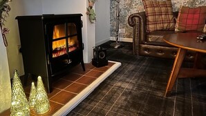A cozy living room with a fireplace, a leather sofa, and a plaid-patterned armchair. - No 4 old Post Office Row, Isle of Skye (Skeabost)