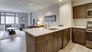 A modern kitchen with a large island, wooden cabinets, and stainless steel appliances. - Sojourn | Courtland Towers | 2 BR (Arlington)
