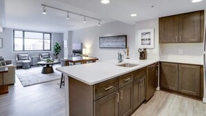 A modern kitchen with a large island, wooden cabinets, and a dining area with a sofa and coffee table. - Sojourn | Courtland Towers Metro Accessible (Arlington)