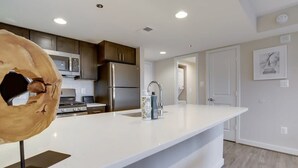 A modern kitchen with stainless steel appliances, a white countertop, and wooden cabinets. - Sojourn | Courtland Towers Metro Accessible (Arlington)
