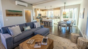 A spacious living room with a grey sofa, a coffee table with books, and a dining area with a table and chairs. - Shell Yeah! - Oyhut Bay Seaside Village (Ocean Shores)