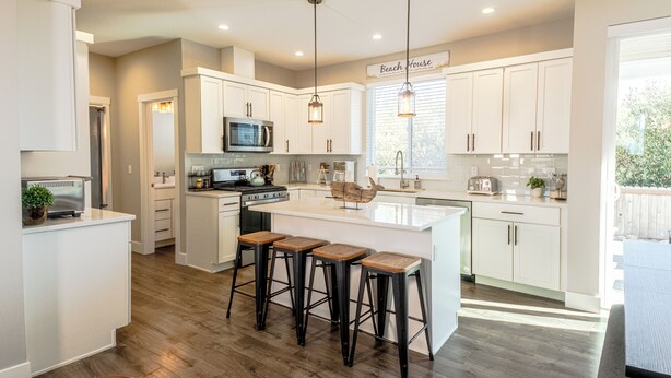 A modern kitchen with white cabinets, a central island with stools, a microwave, stove, and a large window. - Shell Yeah! - Oyhut Bay Seaside Village (Ocean Shores)