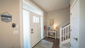 A hallway with a white door, a small console table with a lamp, and a wall-mounted sign. - Shell Yeah! - Oyhut Bay Seaside Village (Ocean Shores)