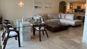 A modern living room with a glass coffee table, a sofa, and a dining area with chairs.