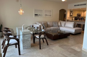 A modern living room with a glass coffee table, a sofa, and a dining area with chairs.