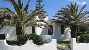 Un edificio blanco con techo de tejas, rodeado de palmeras y un jardín cuidado.