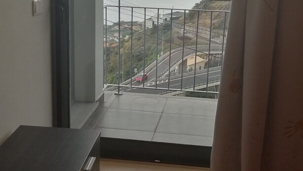 A bedroom with a bed, a nightstand, and a view of a balcony with a railing. - House with nice space near everything (Câmara de Lobos)