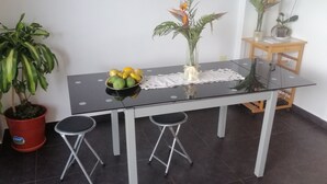A small dining area with a glass table, two stools, a potted plant, a bowl of fruit, and a vase with flowers. - House with nice space near everything (Câmara de Lobos)