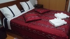 A neatly made bed with red and white bedding, two pillows, and folded towels on a wooden floor. - House with nice space near everything (Câmara de Lobos)