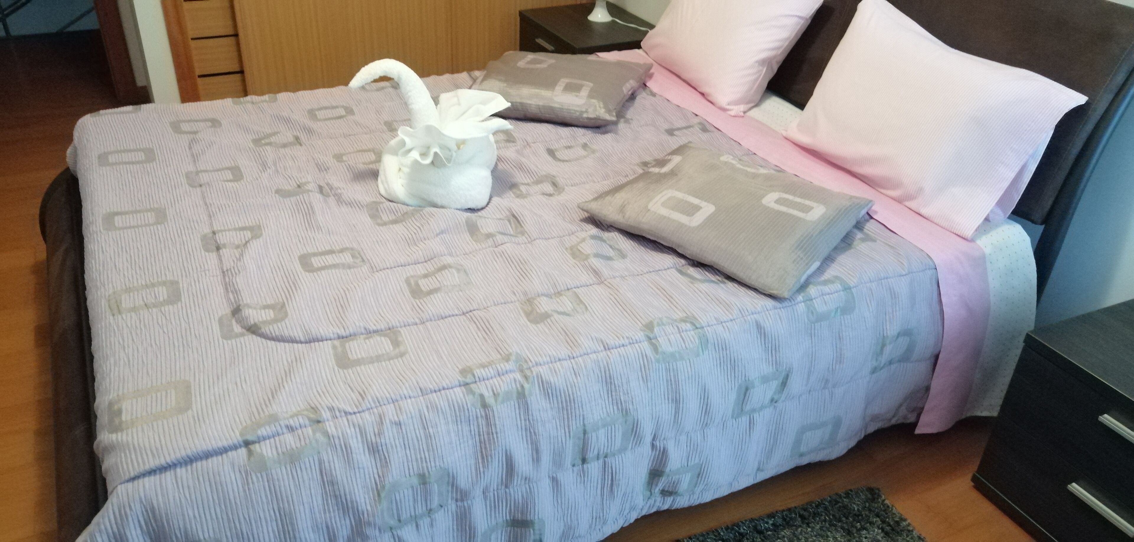 A neatly made bed with a patterned bedspread, pillows, and a decorative swan-shaped pillow.