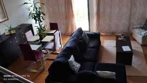A living room with a dark blue sofa, a small table, a chair, a potted plant, a grey armchair, and a TV stand. - House with nice space near everything (Câmara de Lobos)