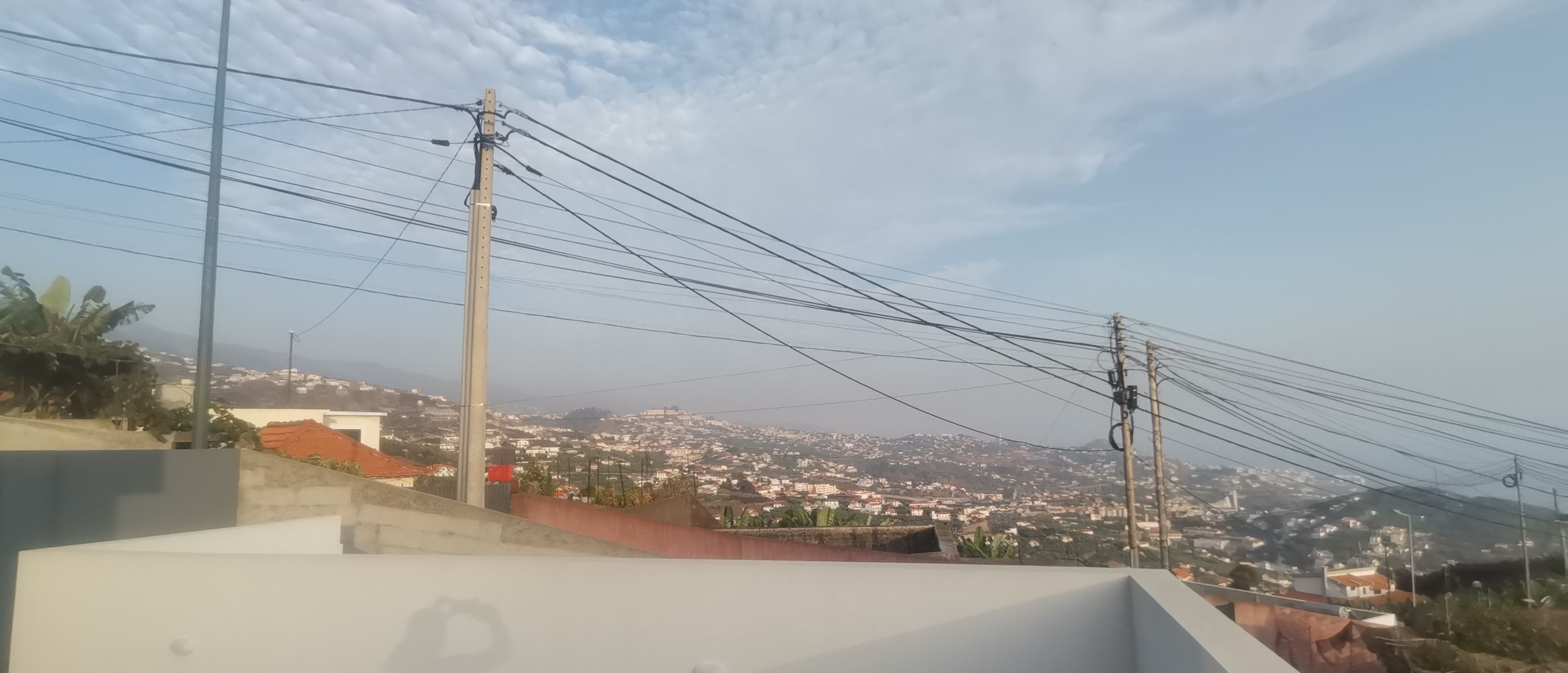 Een dak met uitzicht op een stadsgezicht, elektriciteitskabels en een heldere lucht.