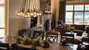 A dining area with a stone fireplace, a large window with a view, and a chandelier. - Luxurious King en Suites in a Pristine Penthouse! (Big Sky)