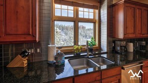 A kitchen with wooden cabinets, a granite countertop, a window with a view of trees, and a coffee maker. - Luxurious King en Suites in a Pristine Penthouse! (Big Sky)