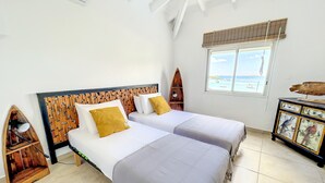 A room with two beds, a wooden headboard, a window with a view, and a cabinet with artwork. - Villa Little Paradise - BIG DISCOUNT MARCH - APRIL !! (Collectivity of Saint Martin)