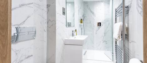 Une salle de bain moderne avec des murs en marbre, une douche en verre et un lavabo blanc.